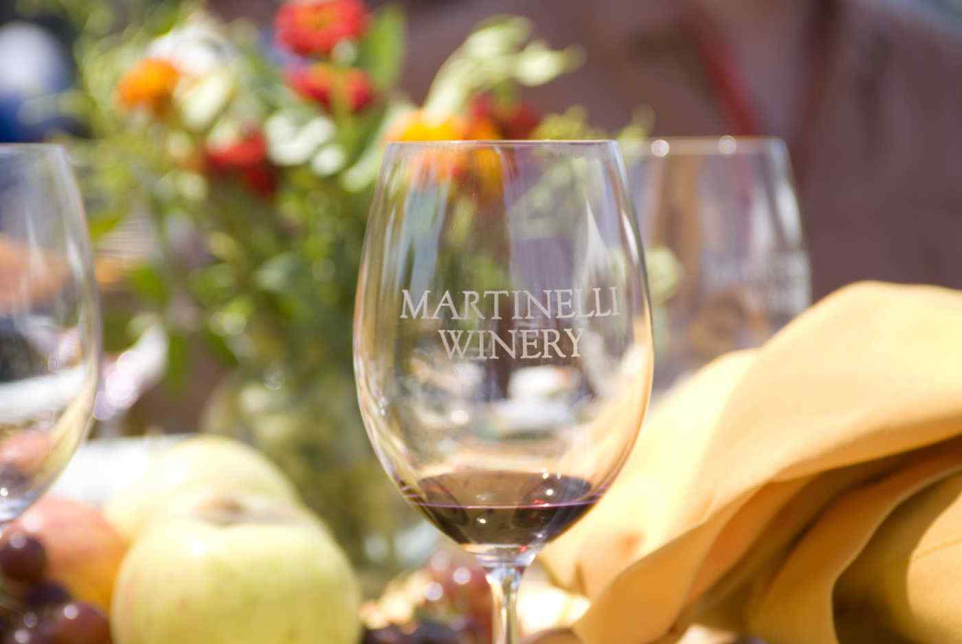 Martinelli winery labeled wine glass with fruit, napkin and flowers in background